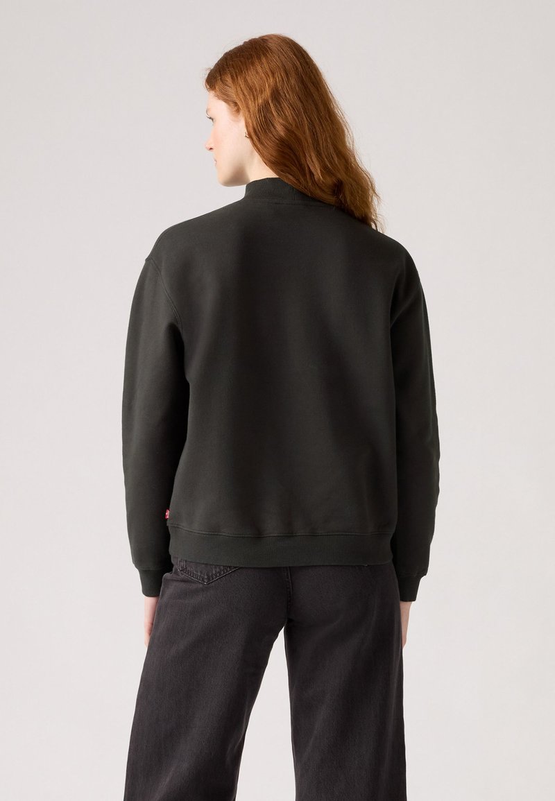 Donkergroen sweatshirt met een hoge halslijn, ribbels aan de manchetten en onderrand. Heeft een zachte textuur; gedragen met donkere jeans. Eenvoudig, minimalistisch ontwerp.