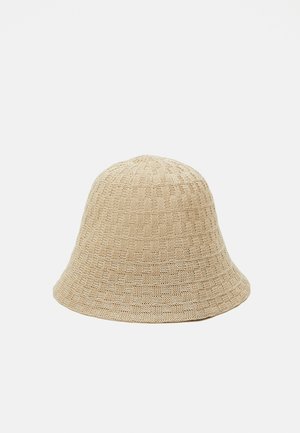 Chapeau seau tissé beige avec un motif texturé subtil et un large bord incliné vers le bas sur un fond clair uni.