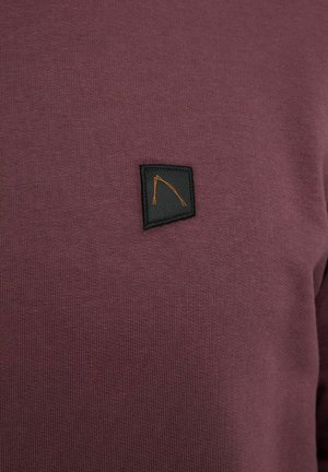 Bordó kötött pulóver, fekete téglalap alakú folttal és narancssárga emblémával, sima textúrával és testhezálló kialakítással.