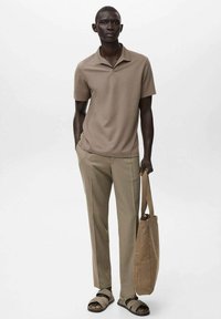 Camisa polo beige con cuello, combinada con pantalones beige claros. Sandalias oscuras y un bolso a juego añaden acentos funcionales.