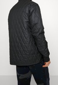 Svart quiltad jacka med hög krage, elastiska manschetter och en slät finish, matchad med mörka, mönstrade träningsbyxor.