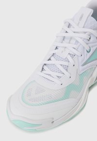 Baskets blanches en tissu mesh, avec des accents turquoise et un design texturé. Elles présentent un bout arrondi et une languette rembourrée avec des lacets.