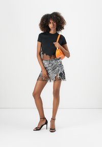Schwarzes kurzes T-Shirt mit gewelltem Saum, gemusterter, transparenter Minirock in Grau und Schwarz, kombiniert mit einer orangefarbenen Umhängetasche und schwarzen Riemchen-Heels.