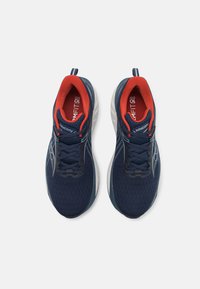 Sötétkék futócipők texturált hálós felsőrésszel, piros belső béléssel, feketefűzőkkel és fehér középtalppal. Saucony márkajelzés jellemzi.