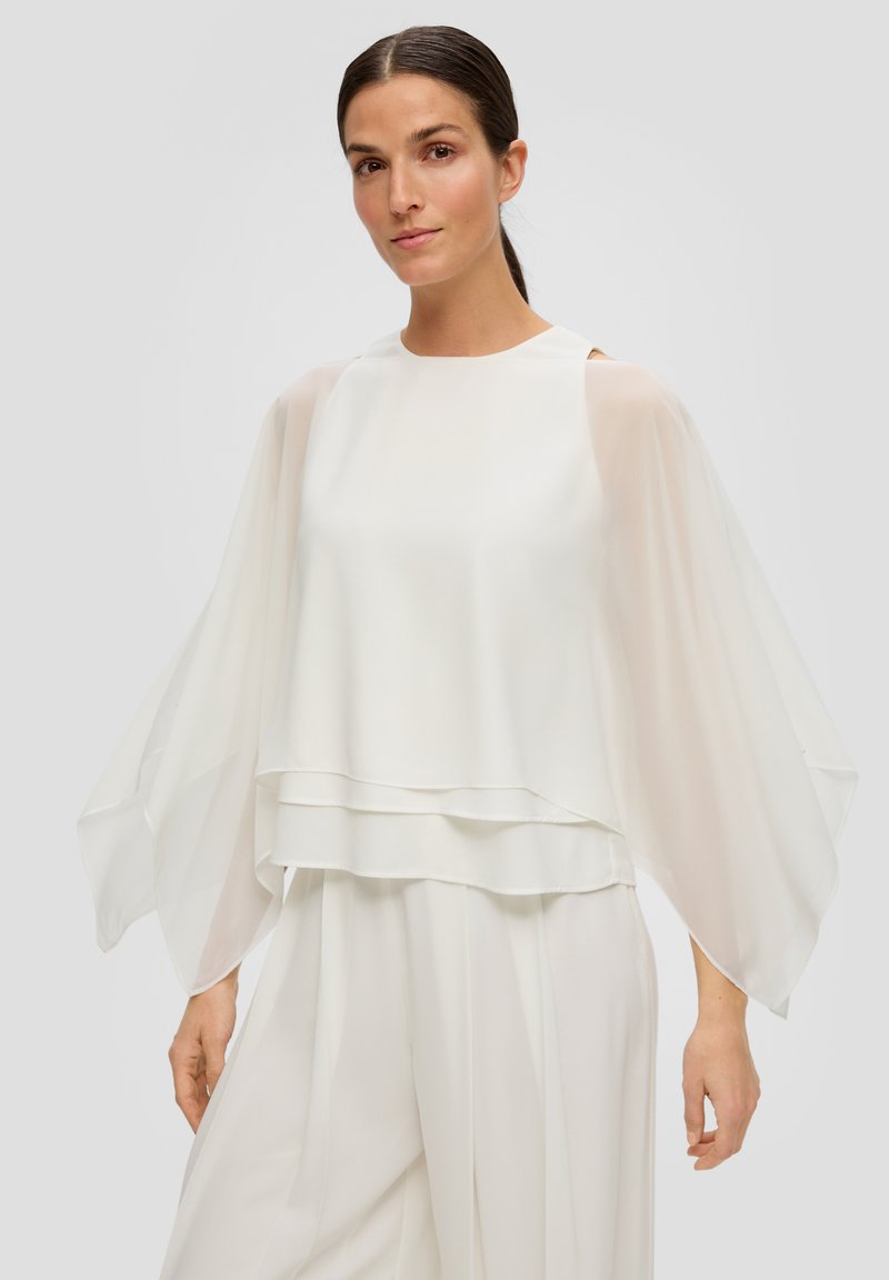 Biała, lekka bluzka z warstwowym wzorem i półprzezroczystymi, zwiewnymi rękawami. Gładka tekstura z okrągłym dekoltem i odkrytymi akcentami na ramionach.