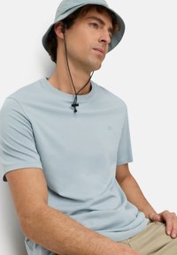 Lichtblauw T-shirt met korte mouwen gemaakt van glad materiaal, met een subtiel logo op de borst, gecombineerd met een blauwe bucket hat.