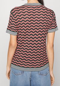 Korte mouw top in een roze en zwart golvend patroon, met een geribde kraag en boorden met een strepenontwerp. Geweven textuur stof.