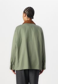 Jachetă supradimensionată verde măslin cu guler din catifea maro, mâneci lungi și o croială lejeră. Material neted cu un finisaj mat.