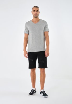 Grå kortærmet V-hals t-shirt, sorte slidte knæ-lange shorts og sorte sneakers med hvide accenter båret af en stående mandlig model.
