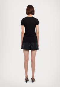 T-shirt nera in cotone con maniche corte e scollo a girocollo, abbinata a pantaloni corti in pelle sintetica nera, indossata con sandali neri con tacco.