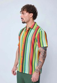 Chemise à manches courtes avec des rayures verticales multicolores en rouge, vert, jaune et bleu, fabriquée en tissu texturé avec un col pointu.