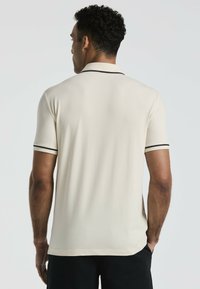 Polo crème à manches courtes, avec un bord noir le long du col et des manches. Texture lisse, coupe décontractée.