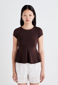 Brown short-sleeve peplum top with a round neckline, made of soft fabric, paired with white cotton shorts featuring eyelet detailing.