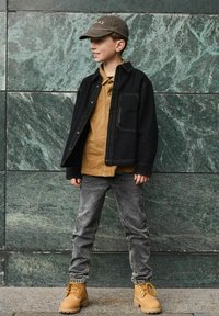 Chaqueta de mezclilla negra, camiseta polo color beige, jeans grises y botas amarillas. Todos los elementos presentan diseños simples con colores y costuras en contraste.