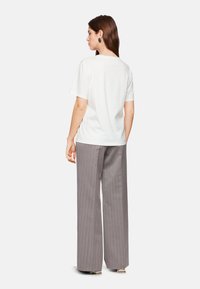 Witte t-shirt met korte mouwen in combinatie met hoge grijze gestreepte broek, met een relaxte pasvorm en zachte katoenen stof.