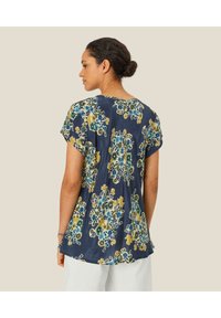 Mørkeblå blomsterbluse med korte ærmer, der har blå og gule mønstre. Let materiale og løs pasform med rund halsudskæring.