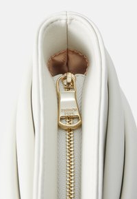 Sac à main zippé blanc avec un extérieur en cuir lisse, des ferrures de fermeture éclair dorées et une doublure en satin douce de couleur beige clair.