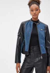 Schwarze Lederjacke und blaue Jeansjacke mit gerippten Schulterakzenten, Reißverschlusstaschen und einer taillierten Passform, kombiniert mit schwarzen hoch taillierten Hosen.