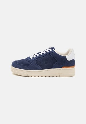 Navy suede low-top sneaker with white laces, beige sole, and tan leather accent on the heel. Features perforated detailing and logo.