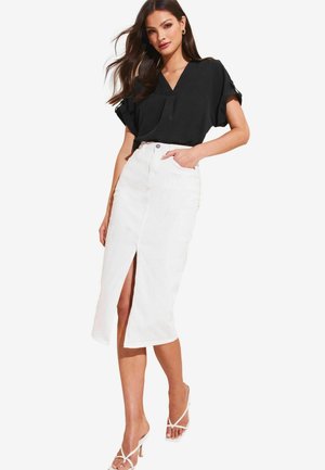 Blusa nera a maniche corte con scollo a V, abbinata a una gonna midi in denim bianca con spacco frontale, completata da sandali bianchi con cinturini.