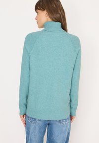 Türkiser Strickpullover mit hohem Kragen und gerippten Bündchen, im lockeren Schnitt mit Raglanärmeln, kombiniert mit hellblauen Denim-Jeans.