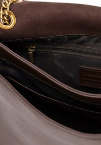 Interiér hnědé semišové tašky s kapsou na zip a látkovým podšívkou, s logem a zlatým řetízkem na vnějším povrchu.