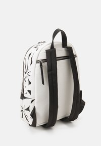 Weißer Rucksack mit schwarzem Blumen-Pergamentdesign, strukturiertem Material, zwei schwarzen Riemen und silbernen Reißverschlussakzenten, ausgestattet mit einer runden Form.