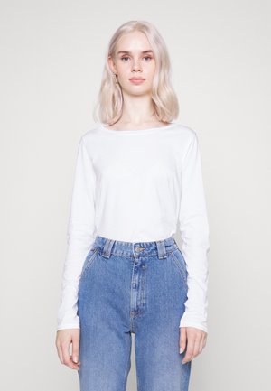 Top in cotone bianco a maniche lunghe abbinato a jeans in denim blu a vita alta con tasche frontali e chiusura con bottoni classica.