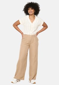 Knit white short-sleeve cardigan with a V-neck and button closure, paired with beige wide-leg striped pants, worn with white sneakers.