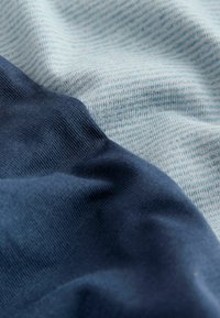 Gros plan sur des plis de tissu doux présentant deux motifs textiles : bleu marine uni et bleu clair avec de fines rayures horizontales.