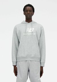 Szary sweatshirt z kapturem, przednią kieszenią i białym logo "New Balance". Materiał wydaje się miękki i teksturowany, z ribbowanymi mankietami i dołem.