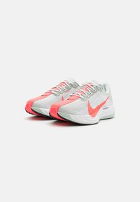 Nike hardloopschoenen met een grijze mesh bovenkant, helderroze accenten, witte zool, veters en een kenmerkend swoosh-logo, met een gestructureerd oppervlak.