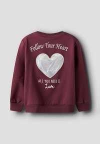 Burgundowa bluza z teksturowanym, błyszczącym wzorem serca na plecach. Biały napis brzmi „Podążaj za swoim sercem” oraz „Wszystko, czego potrzebujesz, to miłość.”