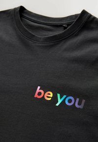 Zwarte katoen T-shirt met een kleurrijke graphic die "be you" in een modern lettertype op de borst afdrukt. Standaard crew neck ontwerp.