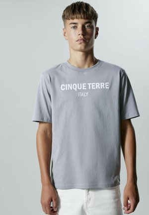 Grå bomullströja med rund halsringning, korta ärmar och vit text "CINQUE TERRE ITALIEN" på framsidan. Avslappnad passform.