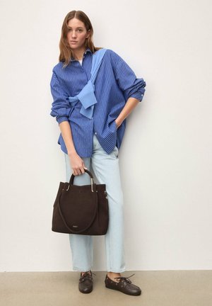 Niebiesko-biała koszula w paski na guziki, jasnoniebieski sweter narzucony na ramiona, jasne dżinsy, brązowa zamszowa torebka i brązowe buty.