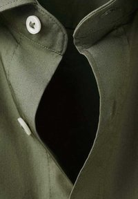 Olivgrüner Hemdblusenkragen mit Knopfverschluss, der eine glatte Textur und saubere Nähte aufweist, aus einem Winkel aufgenommen, um Tiefe zu zeigen.