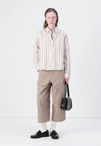 Stripete, lys rosa skjorte med knapper, beige vide bukser, hvite sokker, skinnende svarte loafers og en liten svart håndbag.