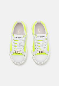 Baskets blanches et jaunes fluo avec une tige en maille, semelle en caoutchouc, design à lacets et accents en or sur les lacets.