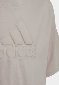 Lichtbeige T-shirt met een getextureerd, verhoogd wit Adidas-logo. Heeft een ronde hals en een subtiel mesh-patroon in de stof.