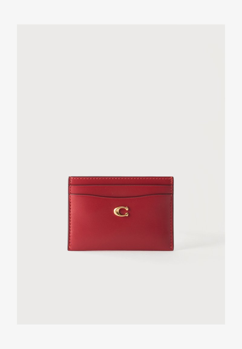 Porte-cartes en cuir rouge avec un emblème doré en forme de lettre C et plusieurs emplacements pour cartes sur un fond clair uni.