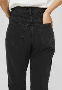 Vaqueros de mezclilla negra con una cintura alta, diseño de cinco bolsillos y bolsillos traseros distintivos con detalles de pespunte.