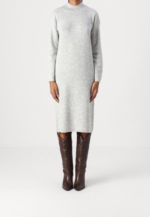 Person wearing a long-sleeve, light gray knit dress paired with knee-high, dark brown textured leather boots.