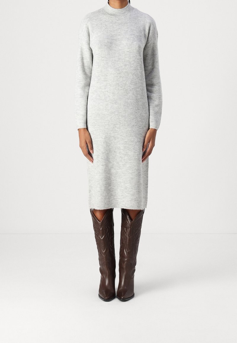 Personne portant une robe en maille gris clair à manches longues associée à des bottes en cuir texturé marron foncé montant jusqu'aux genoux.