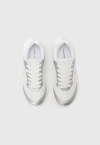 Fehér atlétikai cipők ezüst díszítéssel, texturált kialakítással, lekerekített orral, fehér fűzőkkel és sima gumitalppal.