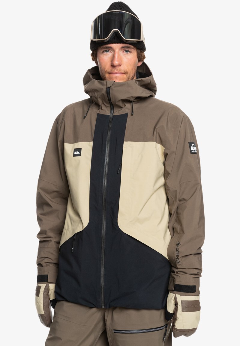 Chaqueta de esquí con un diseño de bloques de color en secciones marrón, beige y negro. Tejido impermeable con capucha y puños ajustables.
