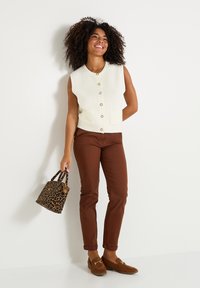Débardeur crème en côtes sans manches avec des boutons sur le devant, associé à un pantalon slim fit marron. Accessoirisé avec un sac en imprimé léopard et des mocassins marron.