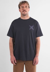 T-shirt en coton noir avec un col rond et des manches courtes. Présente un motif floral violet sur le côté gauche de la poitrine.
