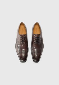 Brune lærdressko med brogue-detaljer, spiss tå og svarte snører. Glatt tekstur med perforerte detaljer og subtil glans.