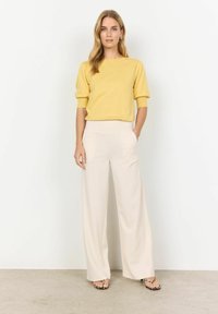 Haut en tricot côtelé jaune avec des manches courtes retroussées, associé à un pantalon large crème taille haute ; tissu léger et doux avec une texture lisse.